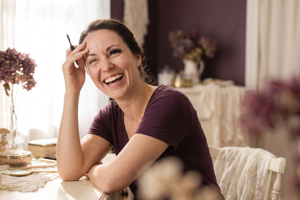 Femme à sa coiffeuse essayant des cils magnétiques pour la première fois, amusée