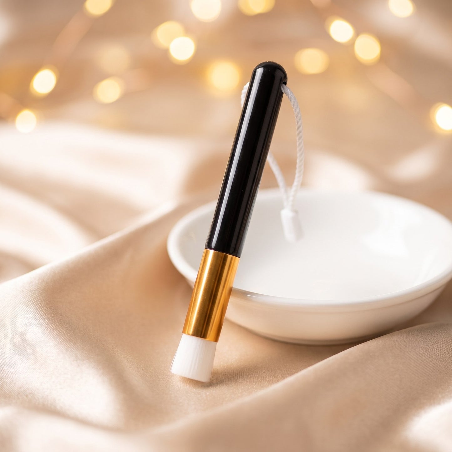 Pinceau nettoyant Cléolya debout sur coupelle blanche, fond satin